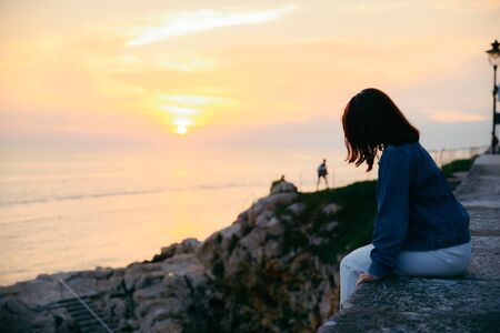 young pretty woman sitting at cliff looking on beautiful sunset. summer travel conceptの写真素材
