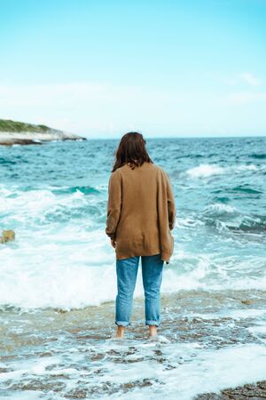 woman walking by rocky sea beach at sunny windy day. summer vacation. carefree concept . waves on backgroundの写真素材