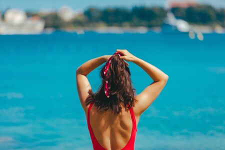 sexy woman in red swimsuit walking into blue clear sea water. summer vacationの写真素材