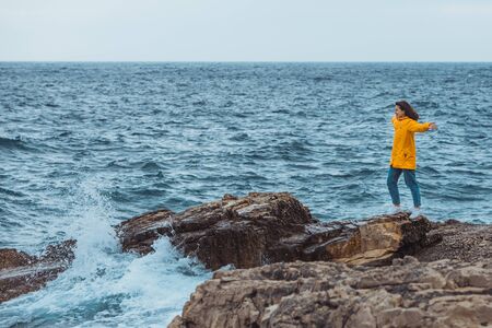 woman enjoying storm weather at sea. rocky seaside