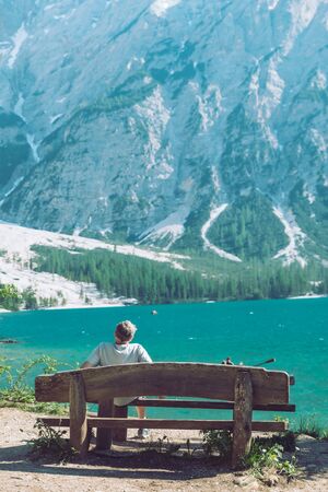 man sitting on the bench enjoying the view of lake in mountains. summer travel concept