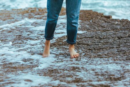 woman walking by rocky beach barefoot wet jeans summer vacationの写真素材