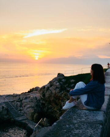 young pretty woman sitting at cliff looking on beautiful sunset. summer travel conceptの写真素材