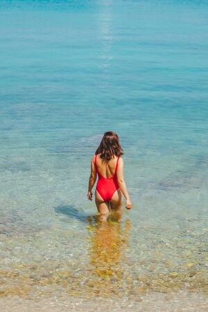 woman standing in sea in the middle in red swimming suit. view from behind. sexy ass. summer vacationの写真素材