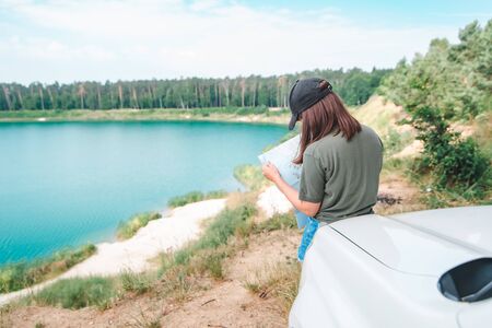 woman checking with map on the suv car hood lake with blue water on background copy space