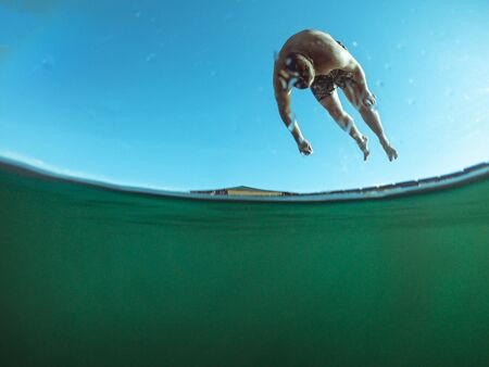 man jumping from wooden pier in lake water summer time