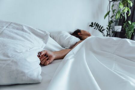 woman sleeping in bed hand close up selective focus white sheetsの写真素材