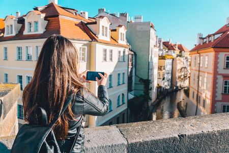 woman taking picture of river canal between buildings on her phone in autumn dayの写真素材