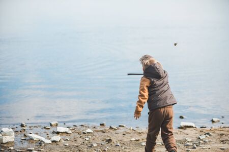 little boy at beach trowing rocks into water. outdoors activitiesの写真素材