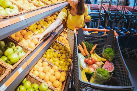 woman taking oranges from supermarket store shelf shopping conceptの写真素材