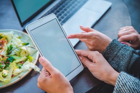 close up view of two women meeting in outdoors cafe working on laptop and tablet no faces