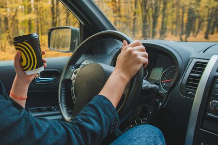 woman driving car by autumn speedway drinking coffee lifestyle road trip