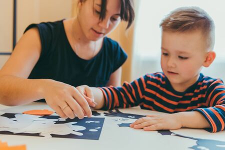 young mother with toddler son making craft spiders for halloween holiday