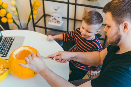 young father with toddler son making jack pumpkin head for halloween holidayの写真素材