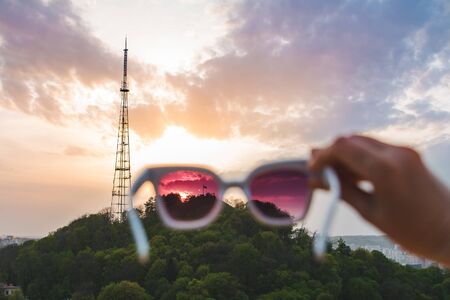 view of sunset in sunglasses holding by handの写真素材