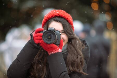 woman photographer with professional camera shooting outdoors at winter time christmas tree on...