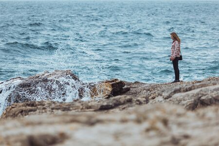 young woman in coat at seaside looking at storming sea. copy spaceの写真素材