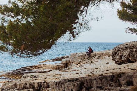 man sitting on rocky beach looking on storming sea. summer travel conceptの写真素材