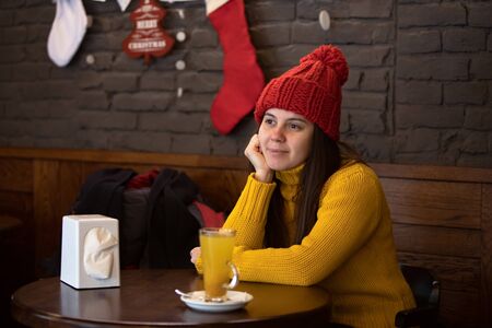 young happy woman in red hat winter outfit sitting in cafe drinking warm up teaの写真素材