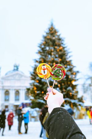 woman hand in red gloves holding candy in front of christmas tree. winter holidaysの写真素材