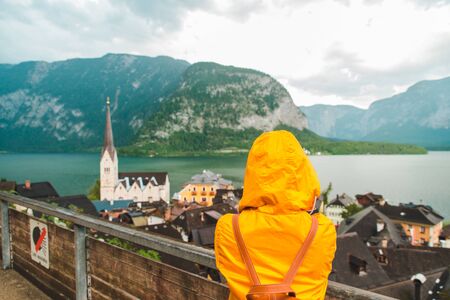 woman in yellow raincoat looking at hallstatt city in overcast rainy weatherの写真素材