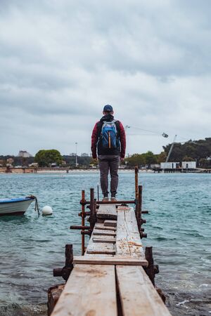 man standing at edge of the small fishing pier looking at stormy sea. overcast weather. sadnessの写真素材