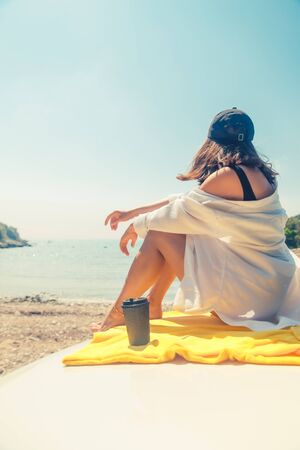 woman sitting at car hood drinking coffee enjoying view of the seaの写真素材