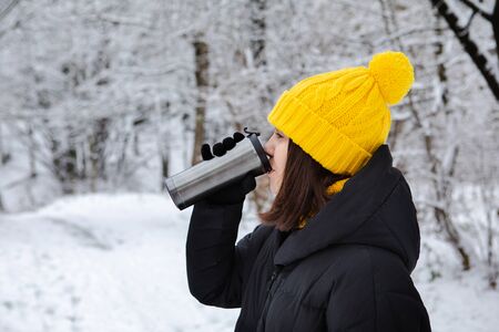 woman in winter outfit drinking warm up drink from refillable mugの写真素材