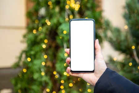 woman hand holding phone with white screen christmas tree on background copy spaceの写真素材