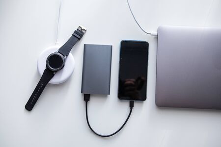 laptop with phone computer mouse and smart watch charging on wireless charger on white table
