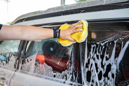 man hand holding yellow sponge cleaning car carwash