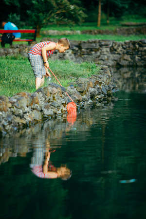 Lviv, Ukraine - June 23, 2019: kid with fish net looking tadpole in lake copy spaceのeditorial素材