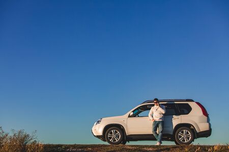 man standing in front of white suv on sunset. car travel concept. golden hours