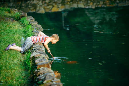 Lviv, Ukraine - June 23, 2019: kid with fish net looking tadpole in lake copy spaceのeditorial素材