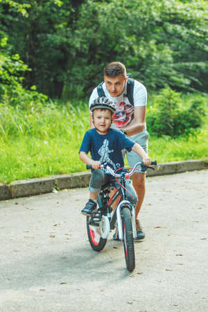 Lviv, Ukraine - June 23, 2019: father teaching son how to ride bicycle. summer time. public parkのeditorial素材