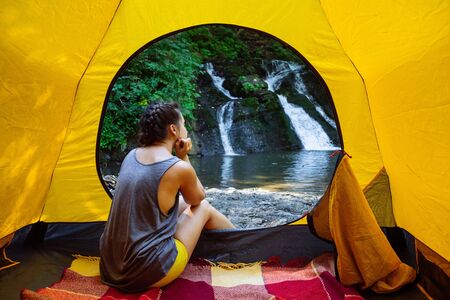 woman sitting in yellow tent looking at waterfall. hiking concept