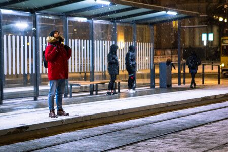 man at winter snowed night at railway station waiting for tram copy spaceの写真素材