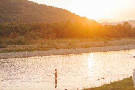 kid with fishing rod standing in river on sunset. copy spaceの写真素材