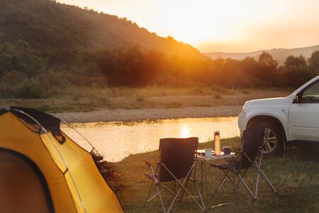 camping at beach of mountain river. suv car. yellow tent. camp table and chairs. copy spaceの写真素材