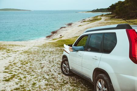 woman legs stick out from car parked at sea beach. summer vacationの写真素材