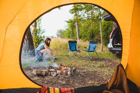 view from camping tent woman cooking on burner near bonfire summer activitiesの写真素材