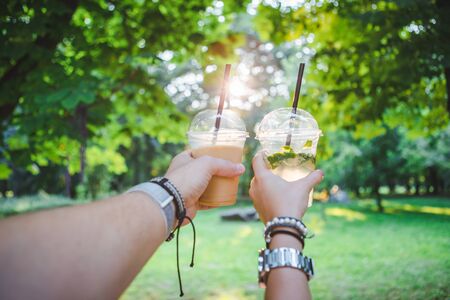 couple hands holding cup with cooling drink. walking by summer public parkの写真素材