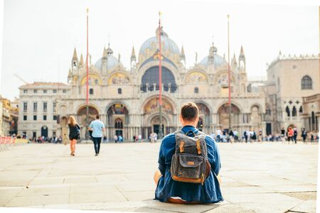 young man sitting on the ground looking at cathedral saint marco basilica copy space. travel conceptの写真素材