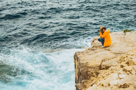 man photographer taking picture on camera standing at the edge of the cliff sea on backgroundの写真素材