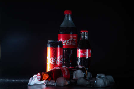 Lviv, Ukraine - 21, 2020: different size bottles of coca cola in ice at black background. flash...