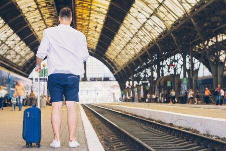 man with suitcase on wheels standing on railway station platform travel concept
