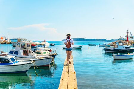 young pretty woman traveler at wooden dock in sea bay. boats on background
