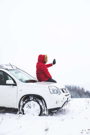 man sitting on car hood and shooting picture of beautiful winter view on his phone. lifestyleの写真素材