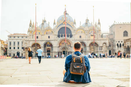 young man sitting on the ground looking at cathedral saint marco basilica copy space. travel conceptの写真素材