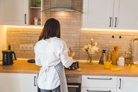view from behind woman on kitchen cookingの写真素材
